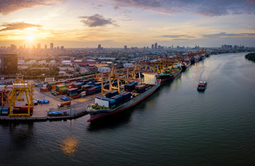 Aerial view of international port with Crane loading containers in import export business logistics with cityscape of Bangkok city Thailand at sunrise