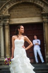 Naklejka premium Wedding photo with the bride and groom. The bride stands epically and looks to the side, and behind her stands the groom near the Catholic Church