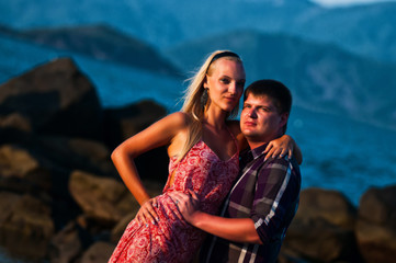 Man and woman sitting on a background of stones, mountains and the sea