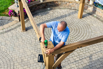 Man building a wooden gazebo on a brick patio - 208947143