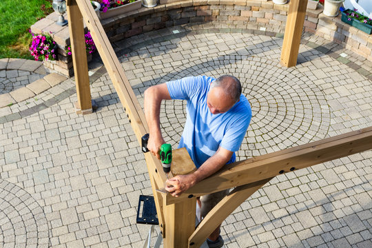 Man building a wooden gazebo on a brick patio
