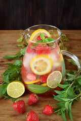 Lemonade with strawberry, lemon, mint, lime and ice cubes in a glass jug surrounded by the ingredients