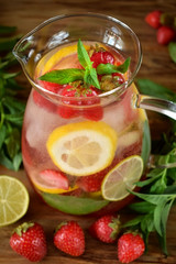 Fototapeta na wymiar Lemonade with strawberry, lemon, mint, lime and ice cubes in a glass jug surrounded by the ingredients