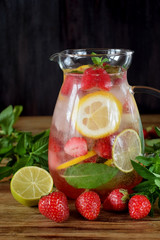 Lemonade with strawberry, lemon, mint, lime and ice cubes in a glass jug surrounded by the ingredients
