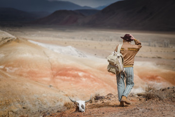 Beautiful young girl in hare, hat and with backpack travels among sands in wild