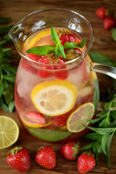 Lemonade with strawberry, lemon, mint, lime and ice cubes in a glass jug surrounded by the ingredients