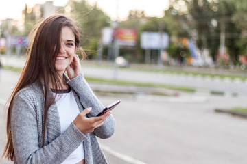 Fototapeta premium Smiling longhair girl using her smartphone at the city street at summer day