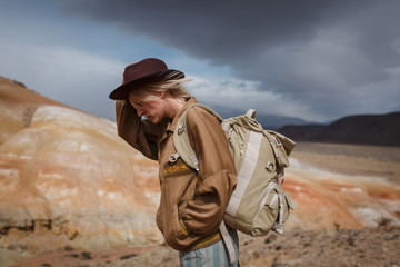 Portrait иeautiful young girl in hare, hat and with backpack travels among sands in wild