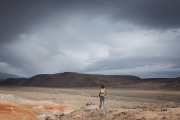 Beautiful young girl in hare, hat and with backpack travels among sands in wild