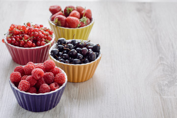 Raspberries, strawberries, currants red and black in colored bowls are on the table