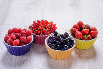 Raspberries, strawberries, currants red and black in colored bowls are on the table