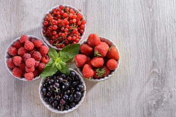 Raspberries, strawberries, currants red and black in colored bowls are on the table