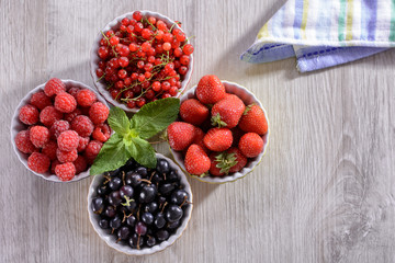 Raspberries, strawberries, currants red and black in colored bowls are on the table
