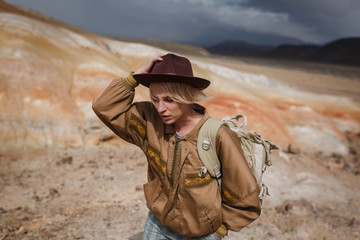 Portrait beautiful young girl in hare, hat and with backpack travels among sands in wild