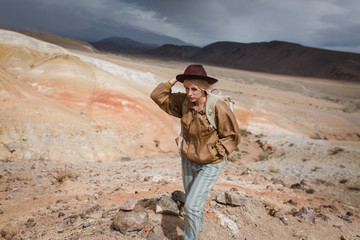 Fototapeta premium Beautiful young girl in hare, hat and with backpack travels among sands in wild