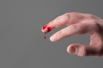 Hand with injured bloody middle finger grey background, copy space. Damage and injury concept. Droplet of blood falling down. Loss of blood and first medical help