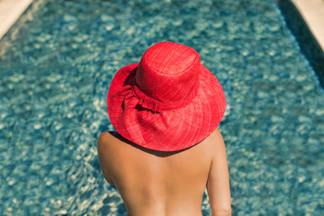 Beautiful young naked woman in a hat in the transparent water of the pool at sunset