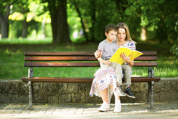 Mother and son in park sitting on a bench and reading book