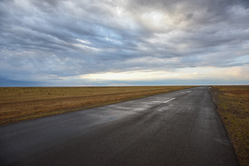 Low angle view of empty wet asphalt road under stormy dramatic sky. Copy space for text or product