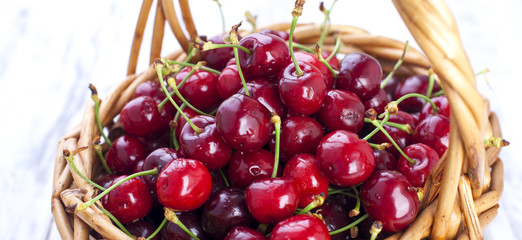 A large basket of ripe cherries. Delicious and sweet berries. White wooden background, free space for text. Copy space. Banner.
