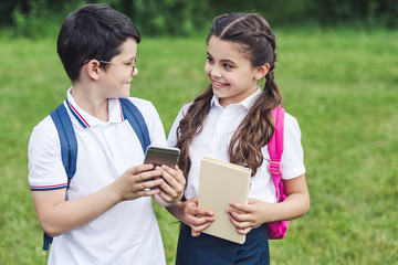 Fototapeta premium smiling schoolchildren using smartphone outdoors together
