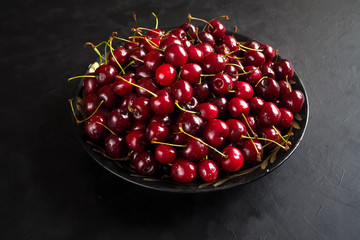 Red cherries in a plate on a black table. Top view. Copy space. 