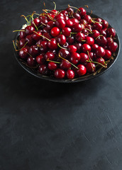 Red cherries in a plate on a black table. Top view. Copy space. 