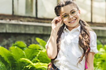 beautiful schoolgirl in uniform and eyeglasses looking at camera in park