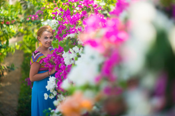 Young beautiful girl posing in a flower garden. The girl is dressed in a blue dress, she is surrounded by purple and white flowers.
