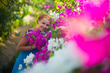 Fototapeta premium Young beautiful woman posing in a flower garden. The girl is dressed in a blue dress, she is surrounded by purple and white flowers.