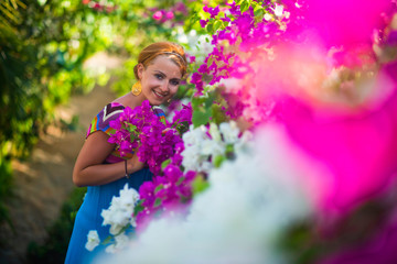 Fototapeta premium Young beautiful woman standing in the middle of flowers. The girl is dressed in a blue dress, she is surrounded by purple and white flowers.