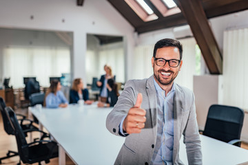 Smiling businessman giving thumbs up in front of his team.