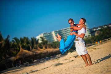 A woman jumps into the arms of a man on the beach on a bright Sunny day against the background of palm trees and sky. The sand flies on the sides