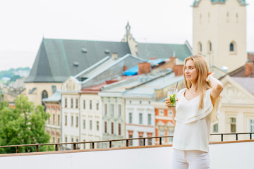 Young woman enjoying great view standing on the terrace of restaurant with soft drink glass..Travel, tourism and resting concept.