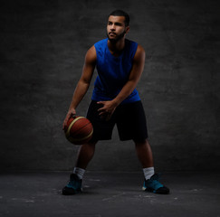 Naklejka premium Young African-American basketball player in sportswear playing with ball. Isolated on a dark background.