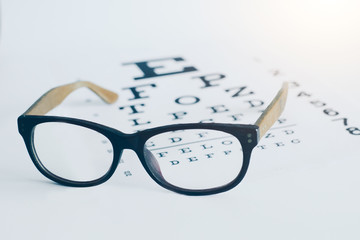 Eyeglasses on an optician visual text chart with white background. Eyesight optician concept - obrazy, fototapety, plakaty