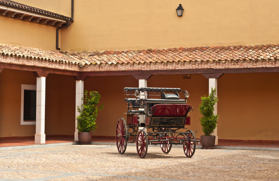 Front view of a horse drawn vintage carriage in the courtyard of a fourth generation winery and vineyard in the southeast region of Spain on a sunny, summer day 