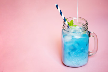Glass of iced Butterfly Pea flower tea with milk on pink background