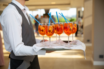 The waiter serves cocktails on a tray. Close-up orange and red cocktails with orange and mint.