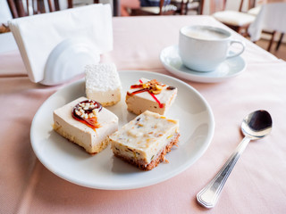 Breakfast in cafe - white cup with cappuccino and plate full of pastries. Tasty desserts and hot coffee.
