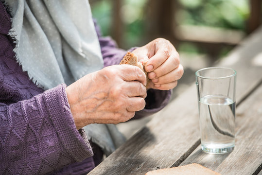 The old woman drinks water and eats bread at an old wooden table in a garden