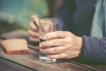 The old woman drinks water and eats bread at an old wooden table in a garden