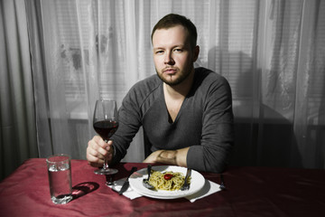 A man drinks wine and eats pasta