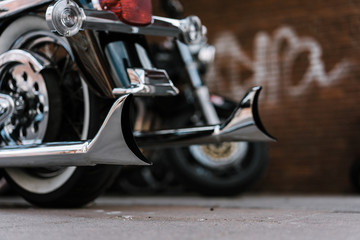 Shiny chromed retro fishtail exhausted pipes of luxury motorcycle. Brick wall with defocused graffiti in background. Soft lighting, vintage look - obrazy, fototapety, plakaty