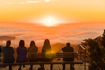 Group of figures watches sunset over clouds filling a forested valley