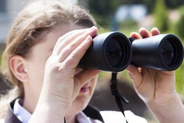 Fototapeta na wymiar A young girl looks through binoculars. The backlight is natural. Bottom view