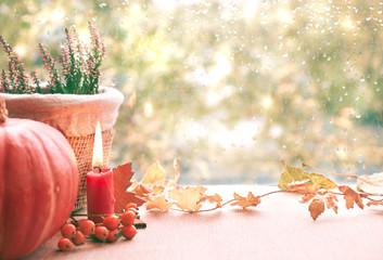 Burning candle, pumpkin, heather and Fall decorations on a window board on a rainy day