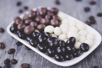Grains of coffee in glaze of white, milky, and dark chocolate. Gray wooden background.