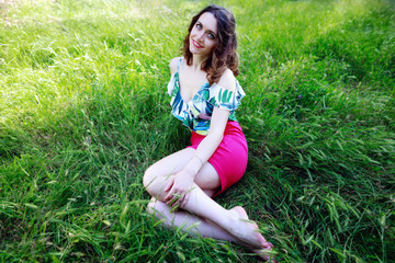 Fototapeta premium Beautiful brunette girl lying in the green grass of the park, looks in camera and smiles.