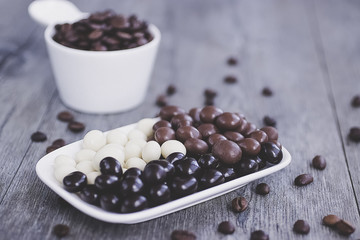 Grains of coffee in glaze of white, milky, and dark chocolate. Gray wooden background.